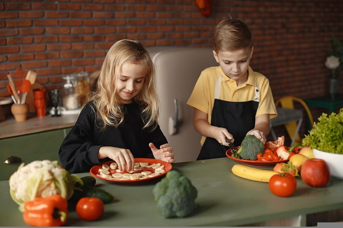 imagem com duas crianças preparando alimentos na cozinha