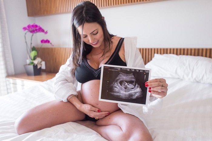 Mulher gestante com uma mão na barriga e a outra segurando a imagem do ultrasom