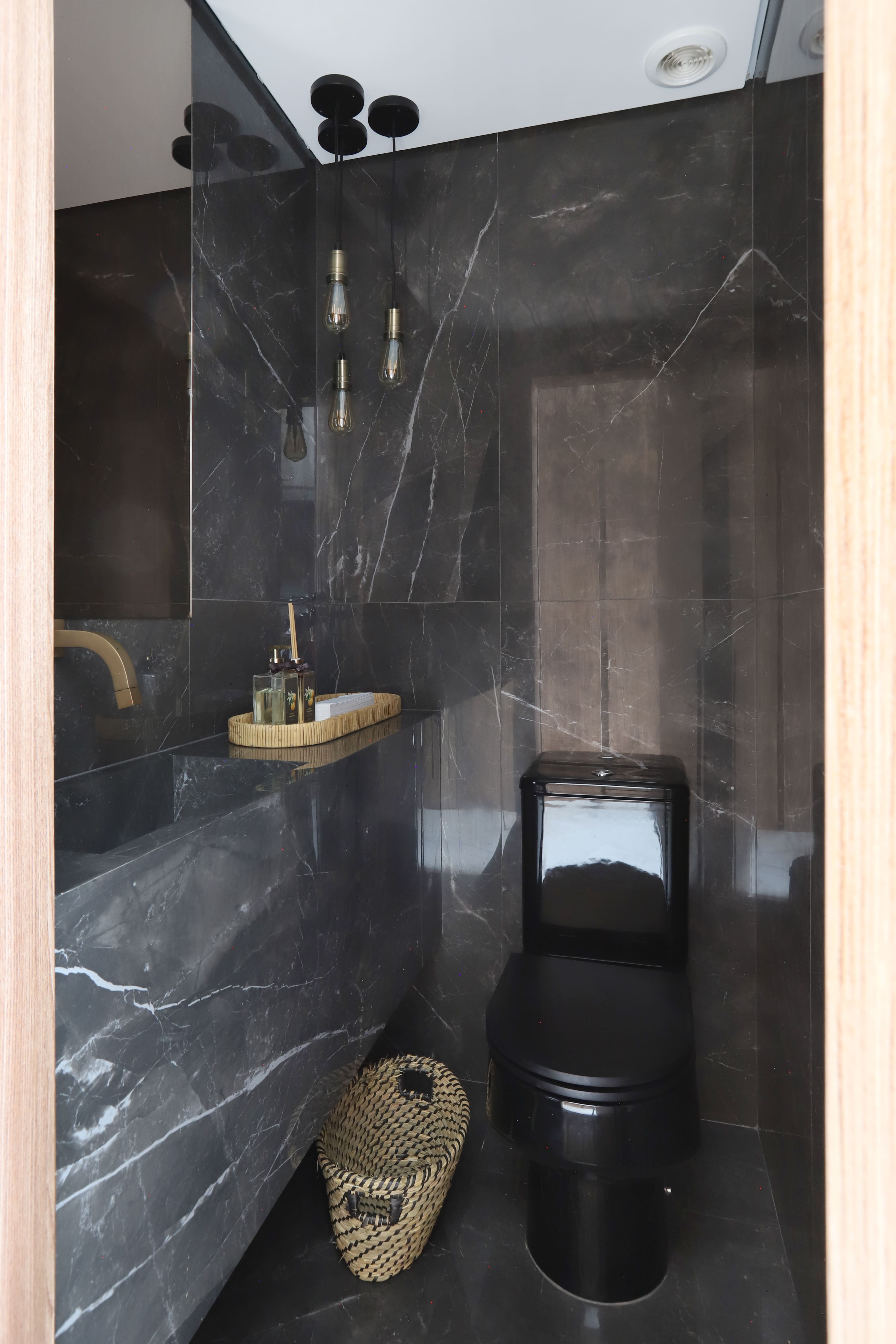 Neste lavabo, a proposta da arquiteta Aiê Tombolato foi surpreender com a sofisticação refletida pelo mármore escuro que forma a bancada com pia esculpida, além de revestir piso e parede.