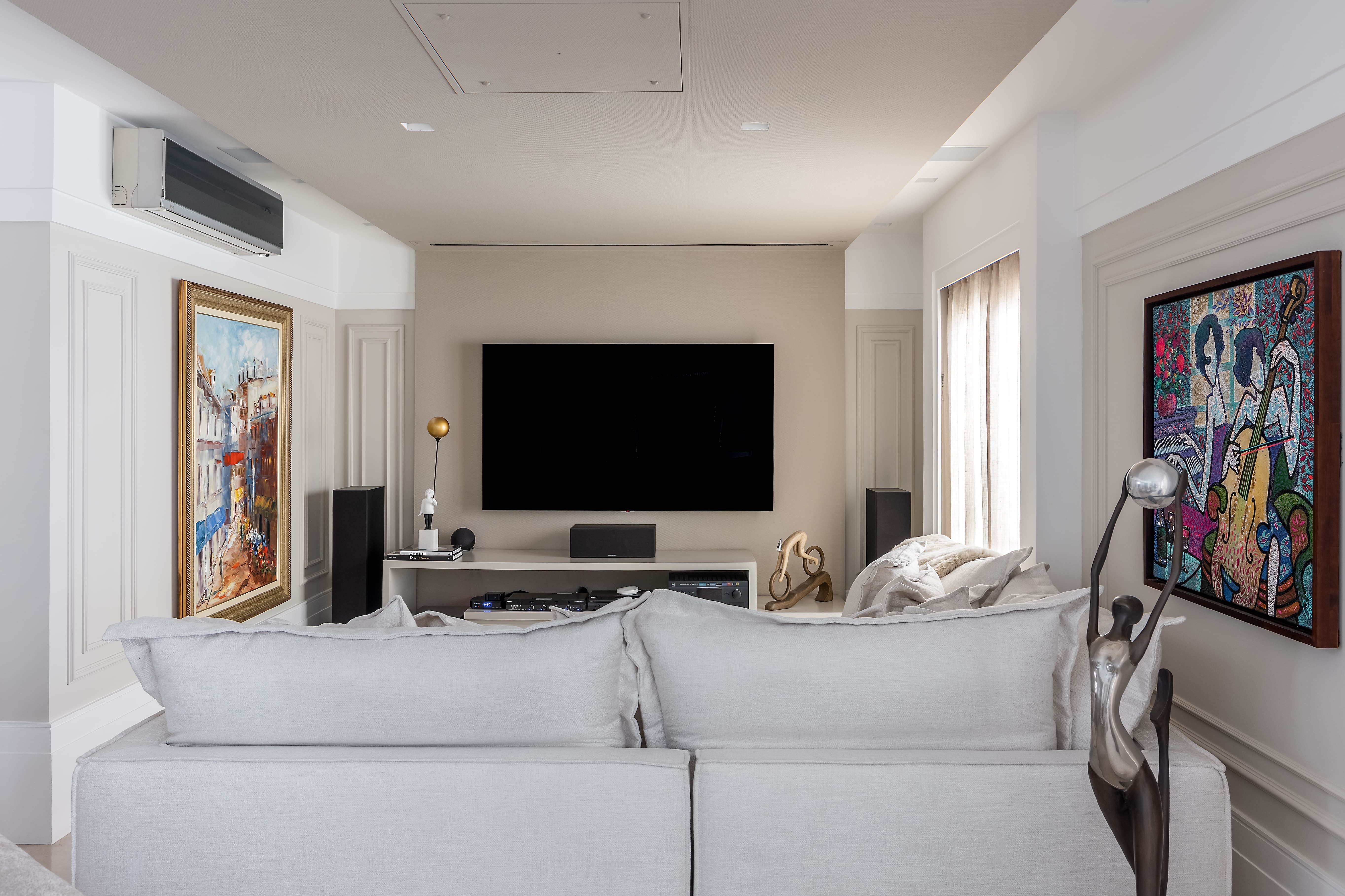 No home theater, o rack com painel que faz um ‘L’ no teto ganhou vida nova com a releitura proposta pela arquiteta.