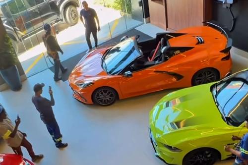 Operários observam e fotografam carros de luxo expostos em uma loja em Vila Velha