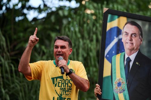 Flávio Bolsonaro (PL) discursa ao lado de retrato do pai, o ex-presidente Jair Bolsonaro, durante evento de campanha em Goiânia